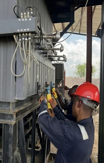 A technician in a red hard hat makes an adjustment to biochar production equipment.